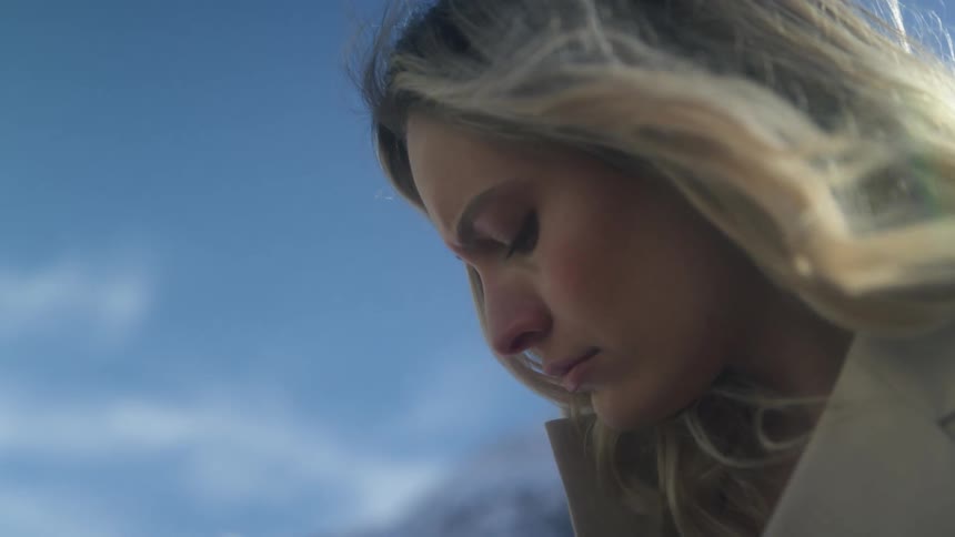 A woman with a jacket with a mountain range the sky and clouds in the background