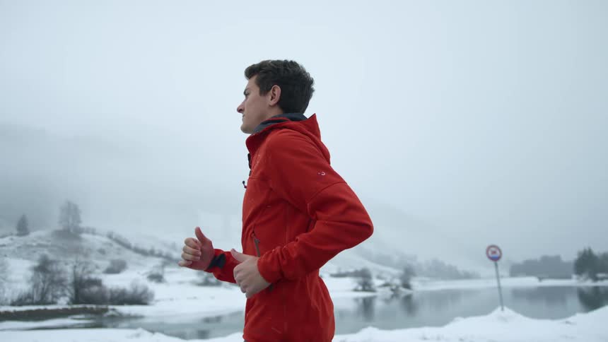 A man jogging next to a lake during a snowstorm in winter