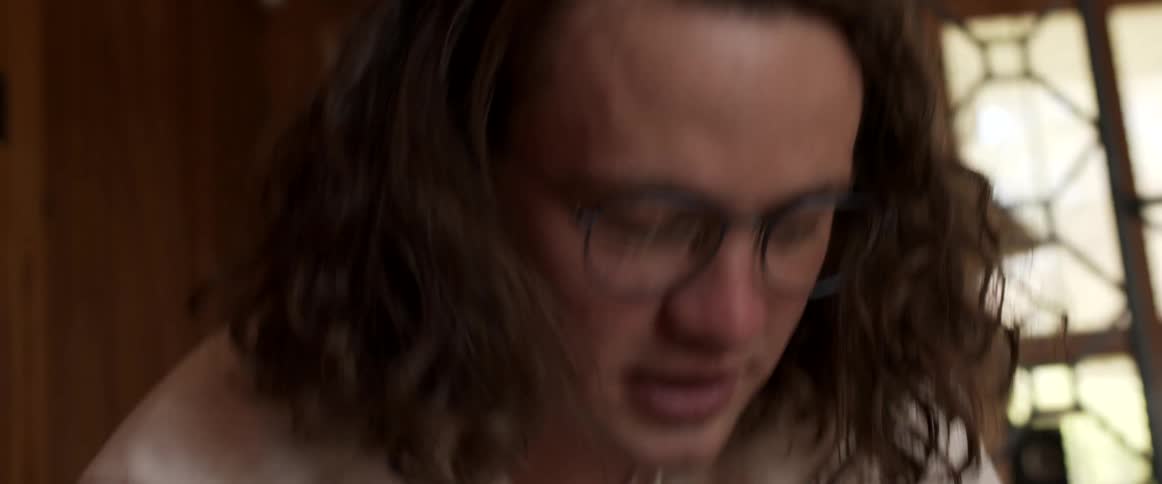 Young man with long curly hair talking to someone in a room