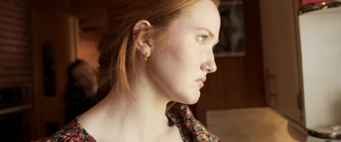 A woman with an upset look on her face standing inside of a moving mobile home staring out a window