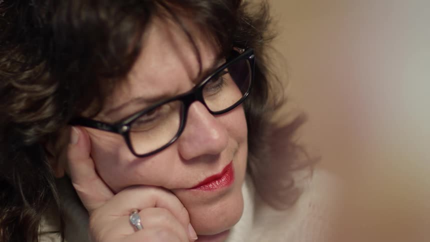 A woman with glasses and a ring in a room with a wall in the background