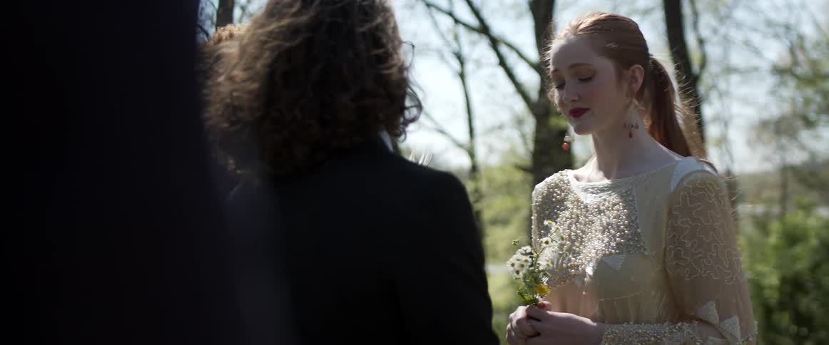 Young pale woman in a wedding dress standing in front of friends outdoors