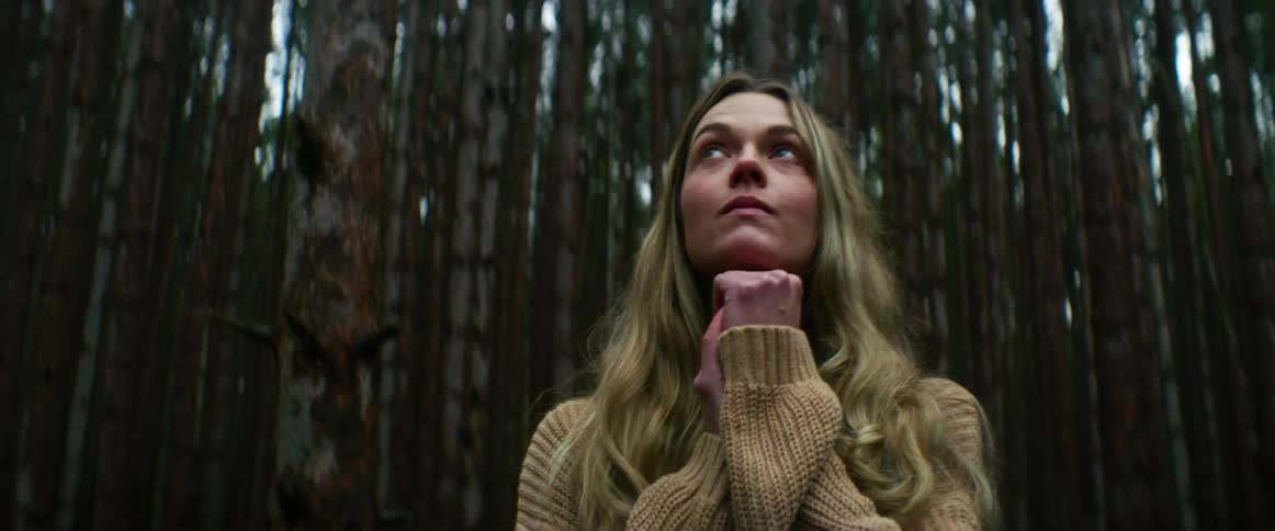 A woman standing in the forest looking around in wonder