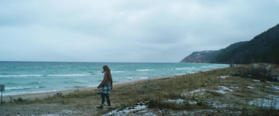 Young woman walking towards the shoreline of a beach next to the ocean