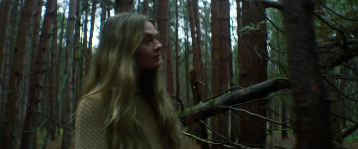 Young blonde woman wearing a sweater walking on the forest