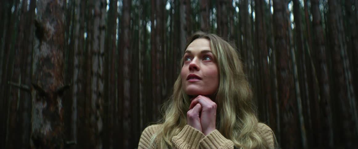 A woman is looking around in the woods