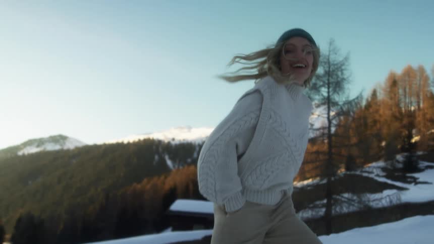 A woman smiling while spinning and walking in snowy mountains