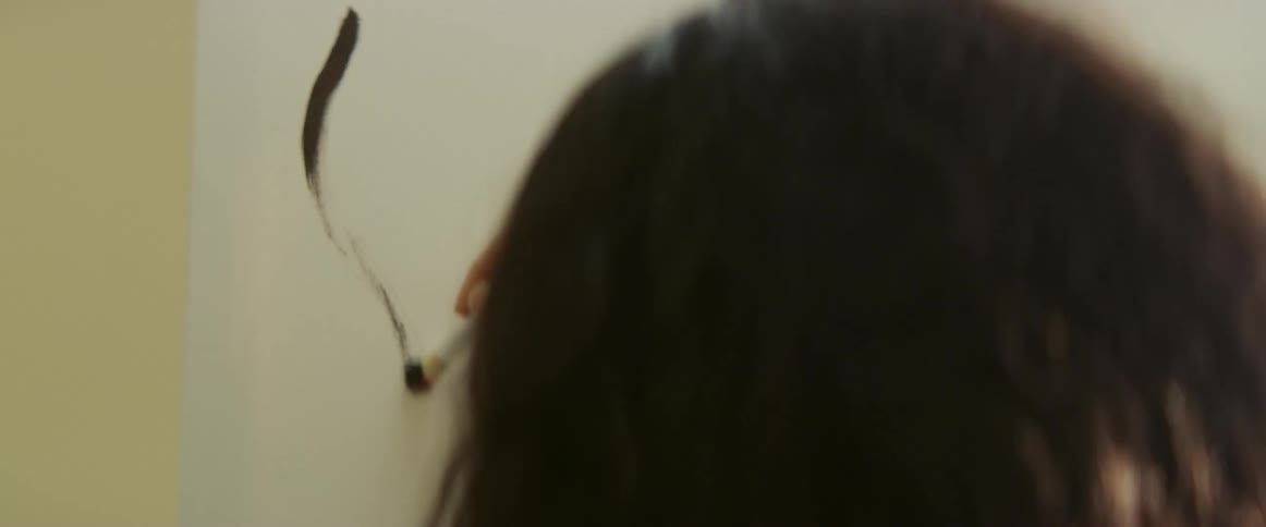 A woman in a room painting on a canvas with a paint brush with a wall in the background