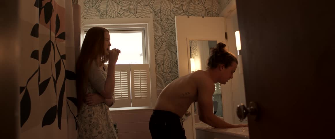 A man and a woman in a bathroom with a wall and window in the background