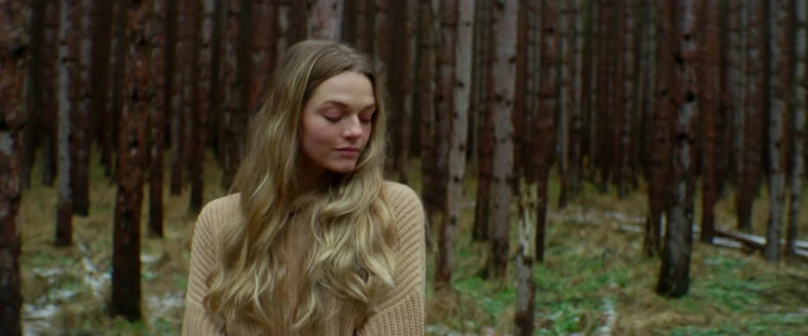 Woman stands in woods with patches of snow on the ground