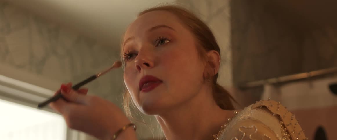A woman in a room putting on makeup with a makeup brush with a wall and doorway in the background