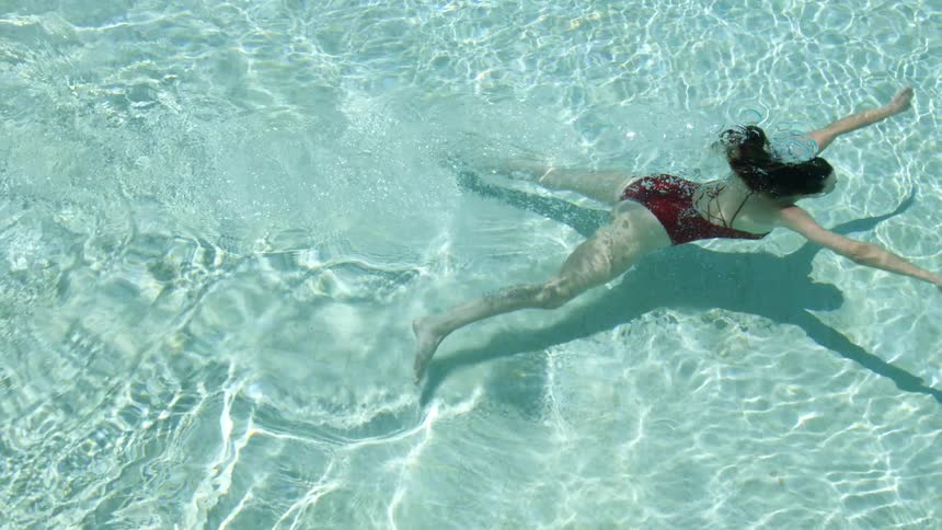 A woman in a bathing suit swimming underwater in a swimming pool
