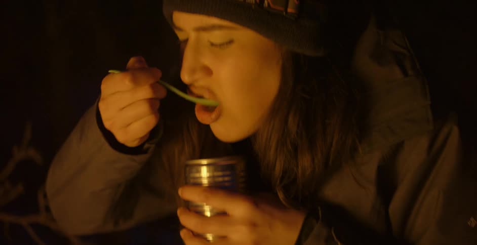 Woman wearing headlampsits outdoors in camp eating