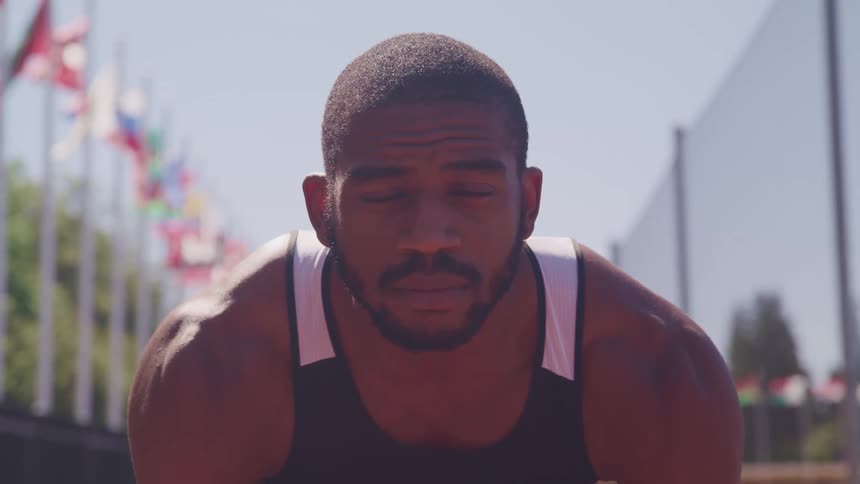 A runner is crouched down before running on a track and slowly looks upwards