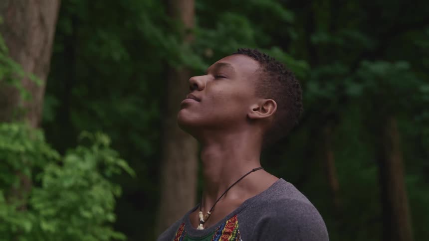 A male hiker closing his eyes while standing still in a forest