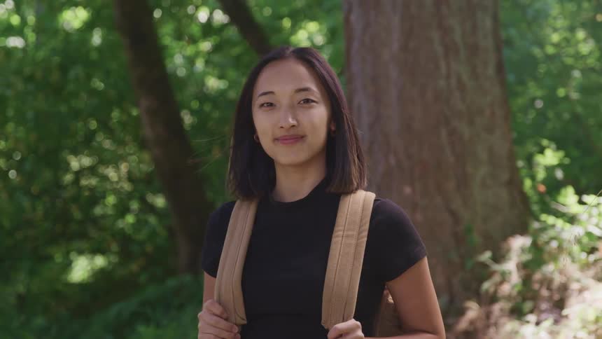 A teenage girl standing in a forest turns her head as he poses for a portrait