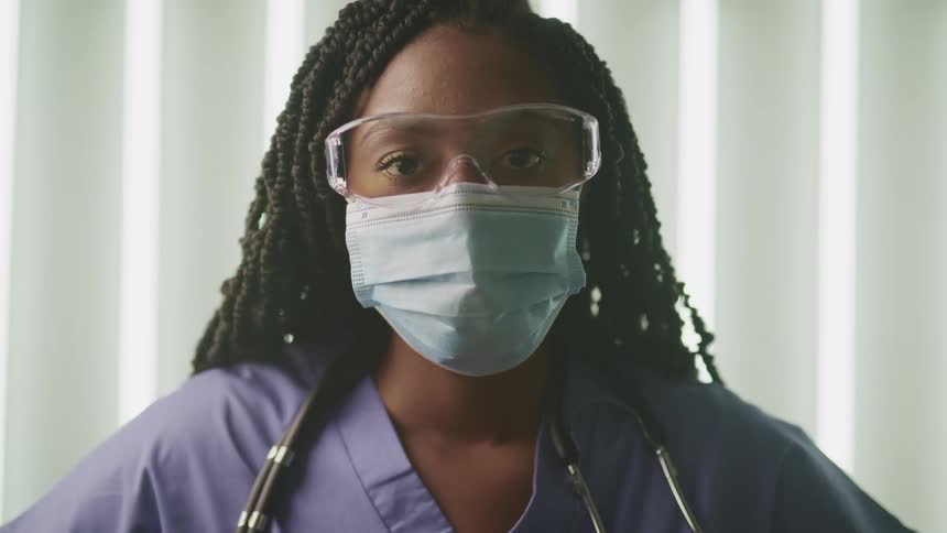 Medical personnel standing in scrubs wears face mask and protective glasses