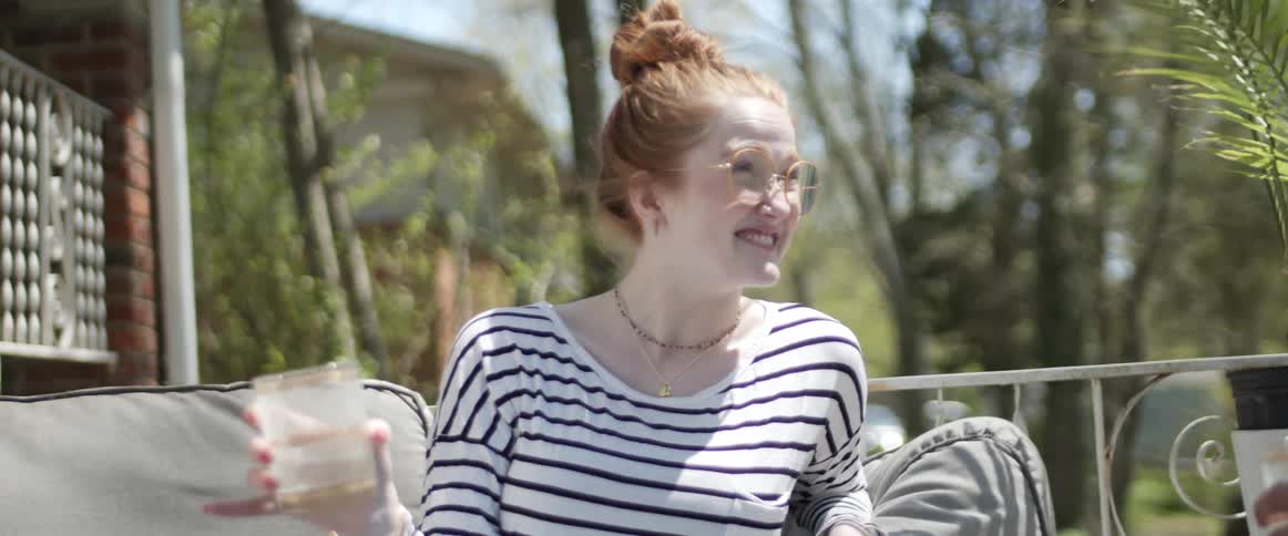 Young pale girl holding a drink in a party talking to friends