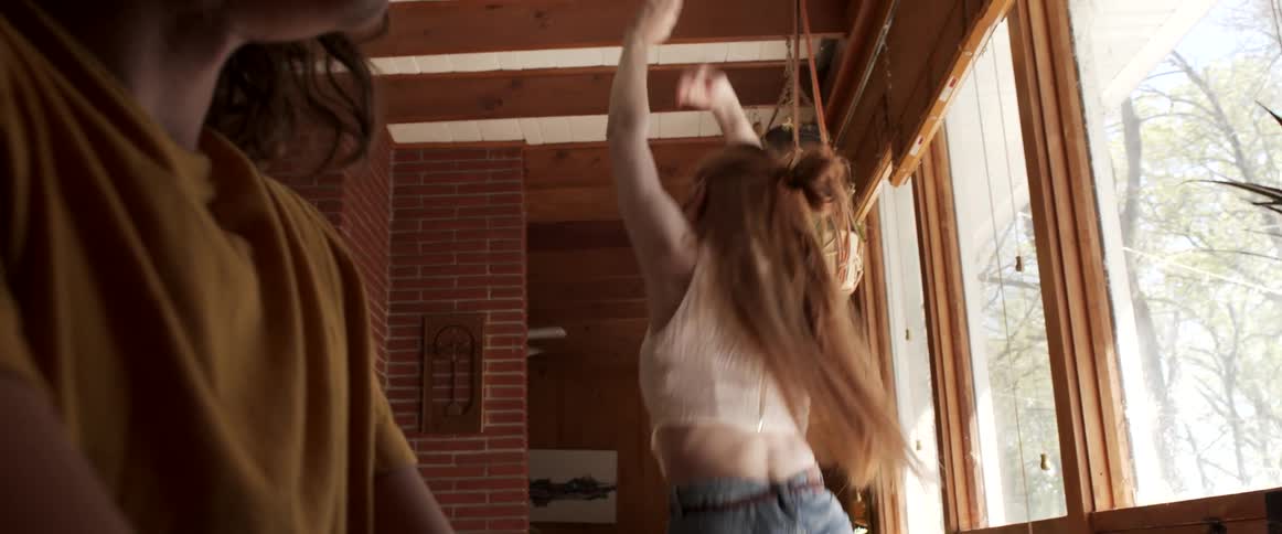 A woman sits at a desk and looks over at the girl who is dancing happily nearby