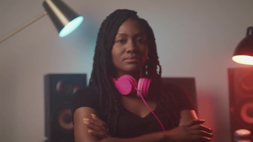 A woman wearing headphones around her neck turns her head and crosses her arms across her chest
