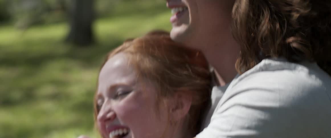 Young couple laughing and talking while hugging on the green grass