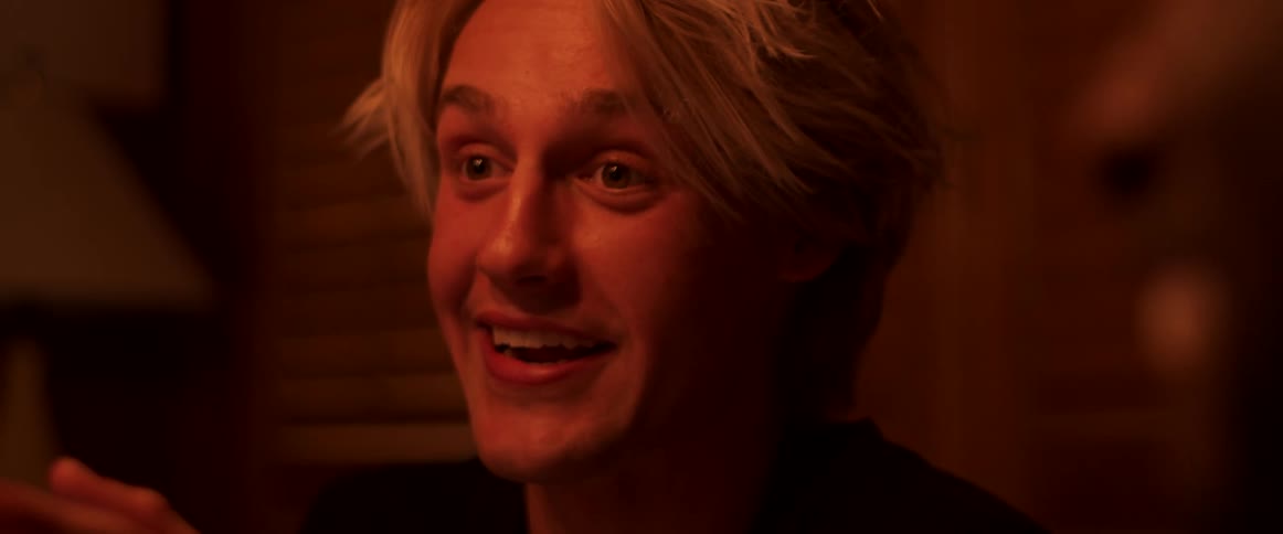 A soft light glows as a man smiles and talks while gesturing with his hand