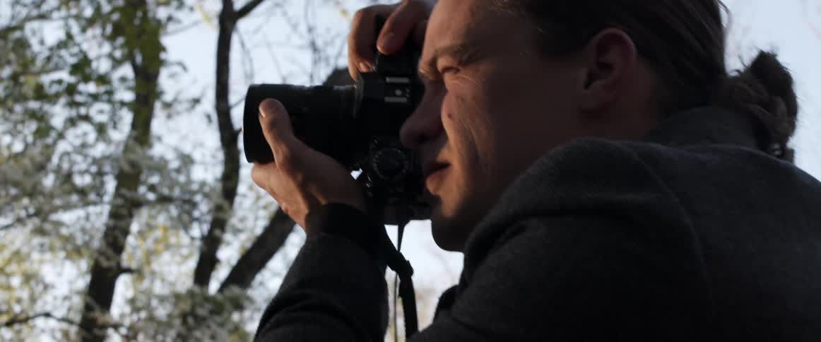 A photographer gives instruction as he quickly takes photographs outside near trees