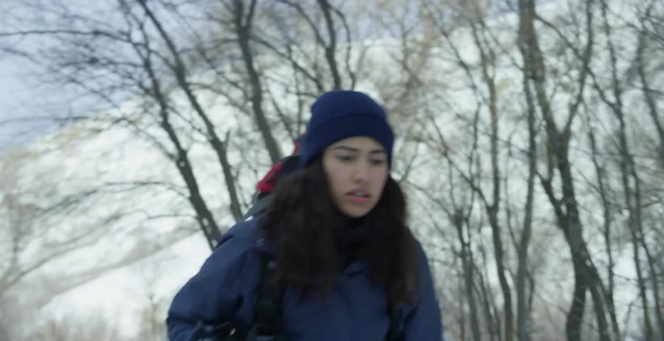 A woman in a coat and winter cap hiking alone in a snowy forest