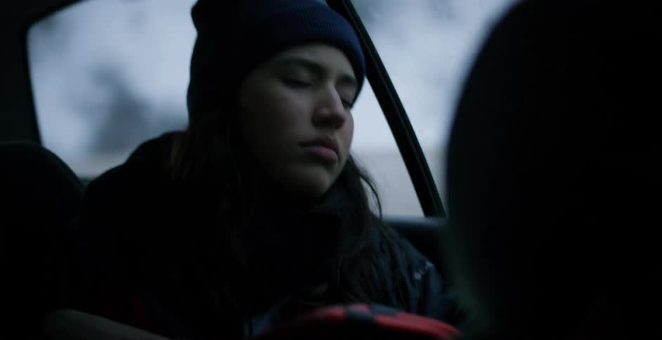 Young woman sleeping in a car driving on a road through the snow covered mountains
