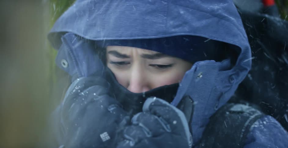 A cold woman shivering outside in a coat during a blizzard