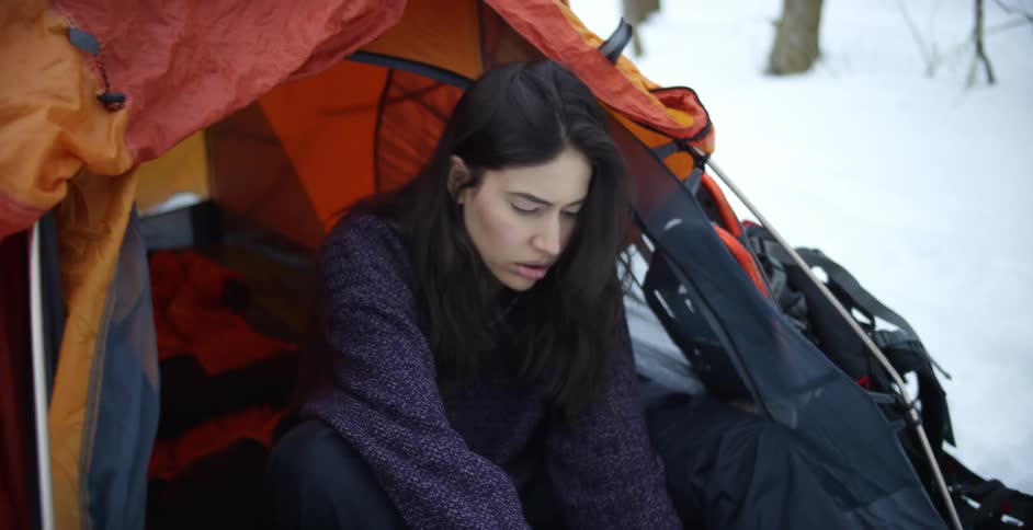 A woman putting on snow boots while sitting in a tent in nature