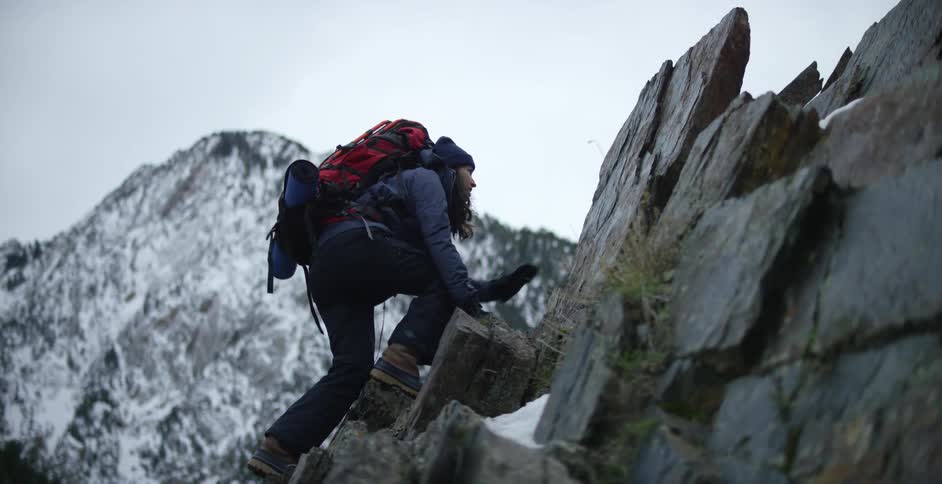 Woman climbs slope with snow covered mountain in background