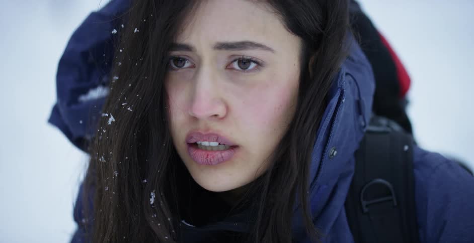 Young pale nervous woman wearing a blue parka with her hair covered in snow