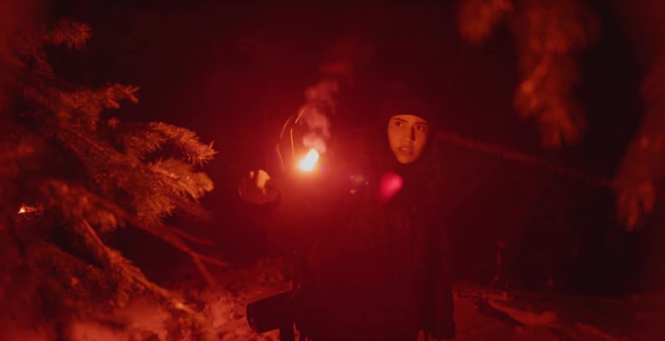 A female hiker looks around a dark forest using a flare at night