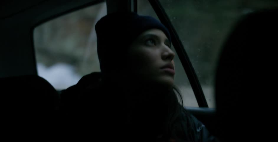 Woman sitting in car looks out window at passing snow covered slopes