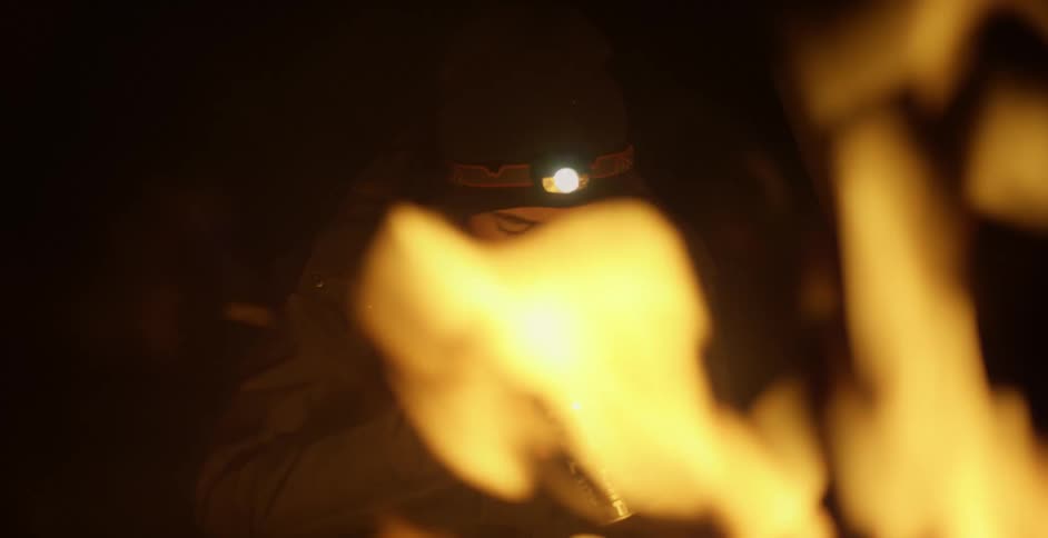 A man sitting by a campfire eating from a can
