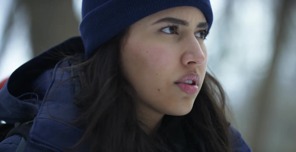 A woman standing outdoors during the day looks down and then up pensive expression on her face