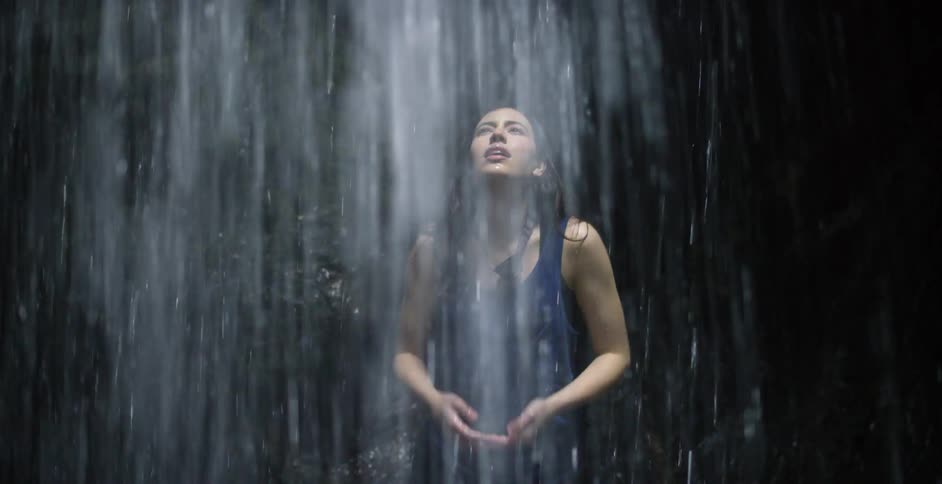 A woman standing underneath a waterfall and splashing water on her face