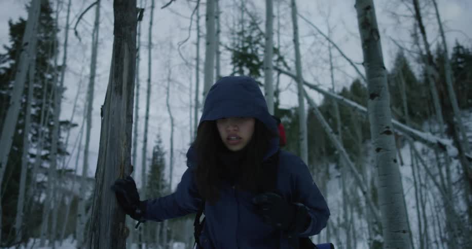 A young woman struggling to walk through a forest in the winter stumbles forward towards the ground
