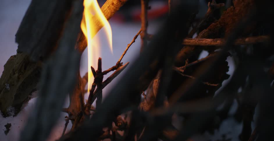 A person starts a fire on a campfire on the snow using a lighter