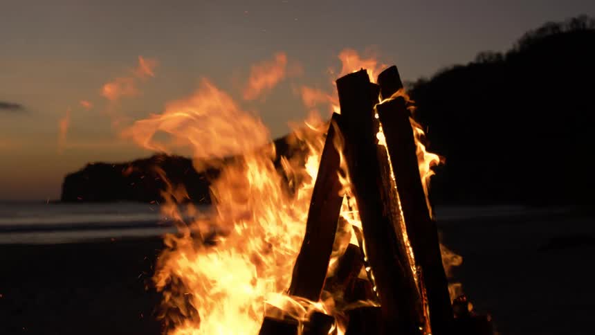 Bright flames from a bonfire on a beach after the sun has set