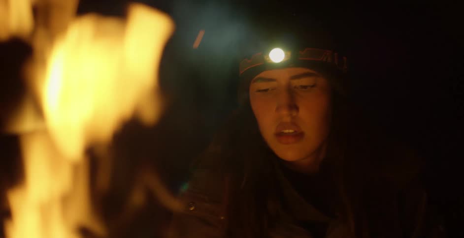A woman with a hat with a flashlight with fire and smoke in the foreground
