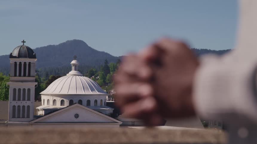 Person prays with clasped hands with churchesand mist covered mountains in background