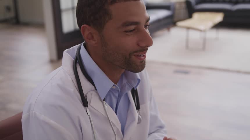 A doctor with a lab coat and a stethoscope with a table and couches in the background