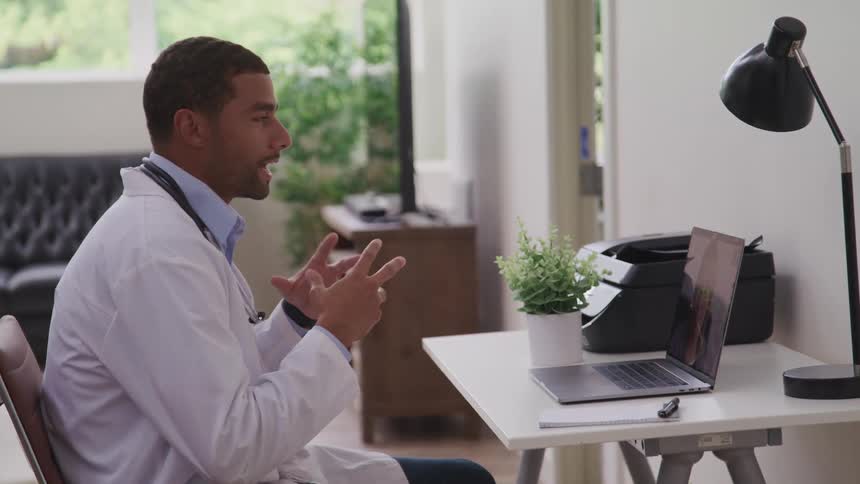A doctor sitting at a desk talking on a laptop