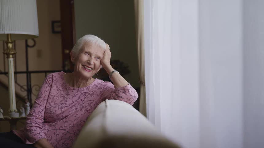 Happy elderly woman smiles while looking out the window of the living room