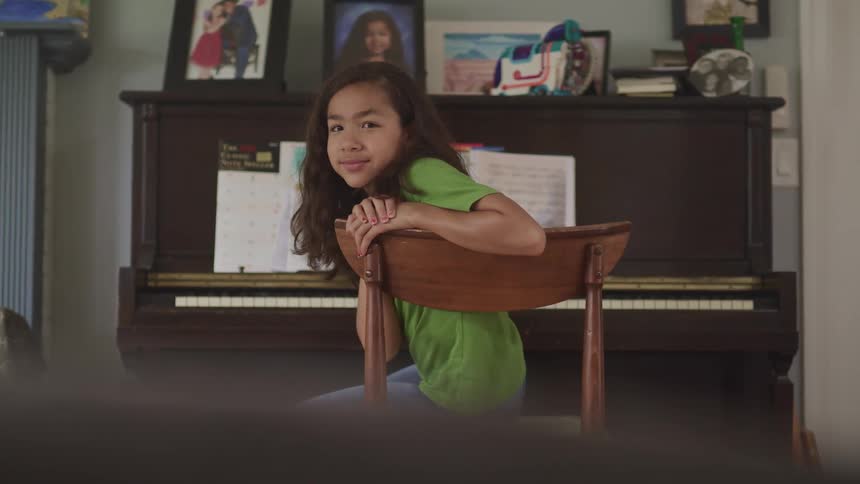 Young girl sitting in front of a piano at home looking at the camera