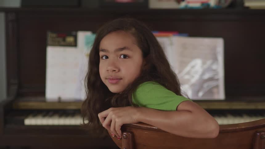 A girl in a room sitting on a chair next to a piano