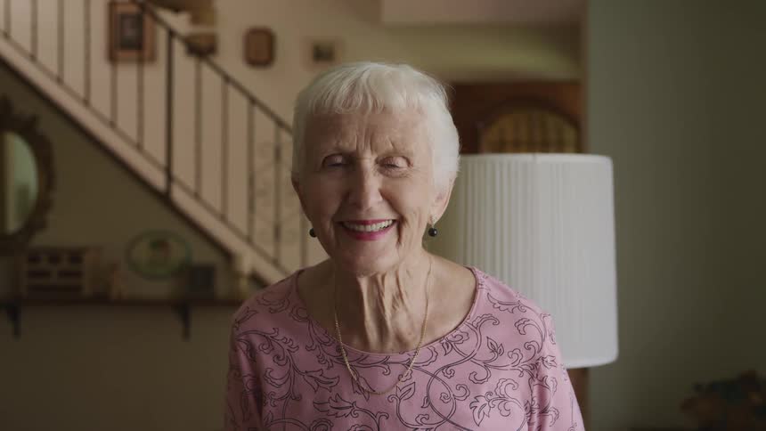 A woman with a necklace in a room with a lamp and a staircase in the background
