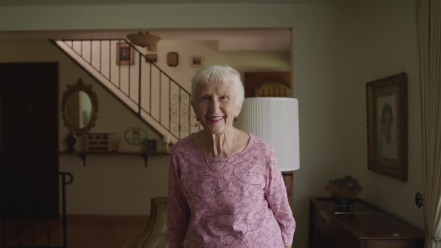 Happy elderly woman standing in the living room at home looks up at the camera